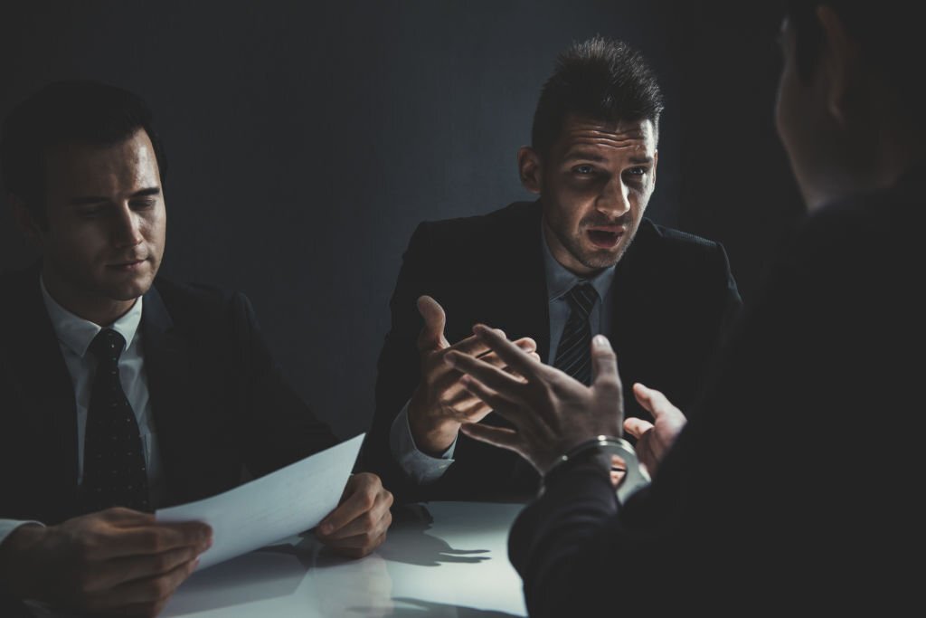 Suspect or criminal man with handcuffs being interviewed by detectives in interrogation room after committed a crime